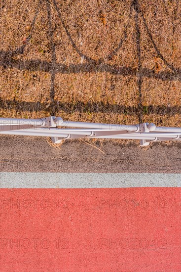 Looking down onto red bike path next to metal guardrail casting its shadow on brown grassy area in South Korea