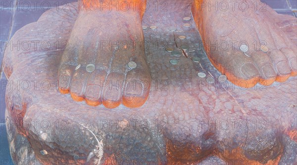 Coins laying on the feet of a wooden statue on top of plinth in South Korea