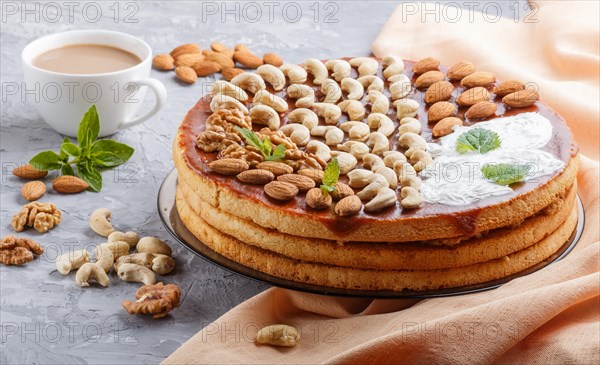 Homemade cake with caramel cream and nuts with cup of coffee on a gray concrete background. side view, close up