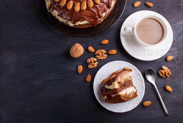 Homemade chocolate cake with milk cream, caramel and almonds on black wooden background. cup of coffee, top view, flat lay, copy space