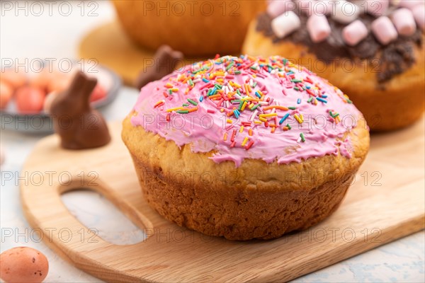 Homemade glazed and decorated easter pies with chocolate eggs and rabbits on a white concrete background and yellow textile. Side view, close up, selective focus