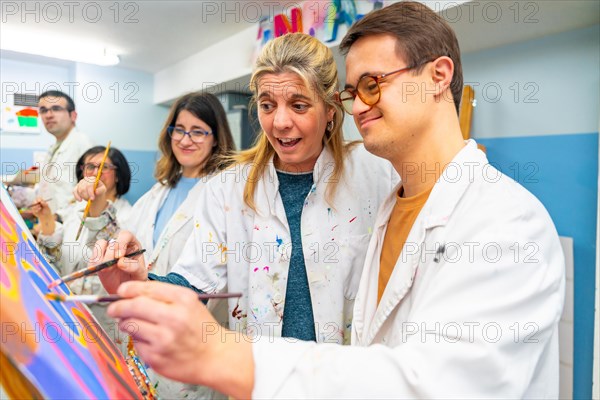 Instructor helping a man with down syndrome to paint on canvas in a painting class