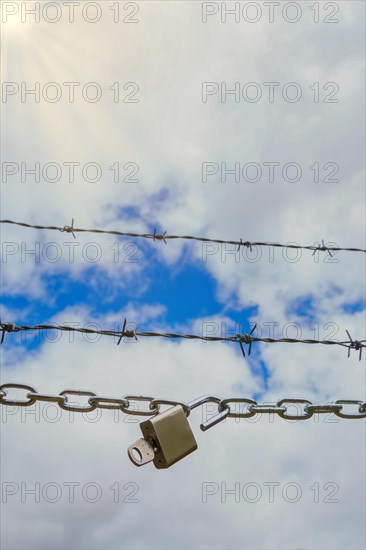 Chain with padlock open with key next to a barbed wire with a blue cloudy sky with sun rays, concept of freedom