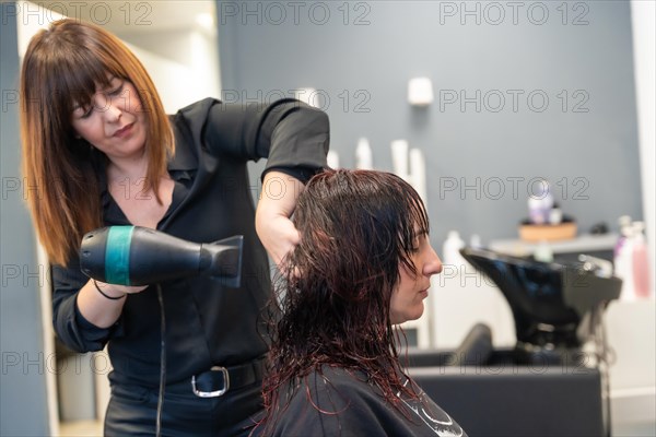 Side view of a mature beauty hairdresser arranging and drying the hair of a client in the salon