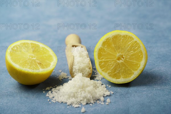 Lemon cut in half with salt on a wooden spoon on a blue background and copy space