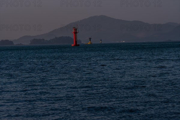 Three small light houses in a harbor with small mountains shrouded in fog and mist in the background in Namhae South Korea