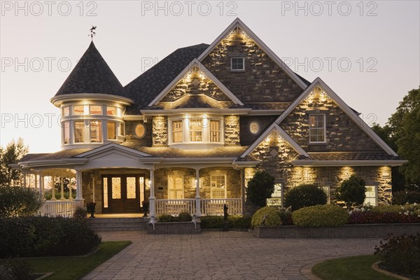 Elegant grey stone with white trim and blue asphalt shingles roof Victorian home facade at dusk in summer, Quebec, Canada, North America