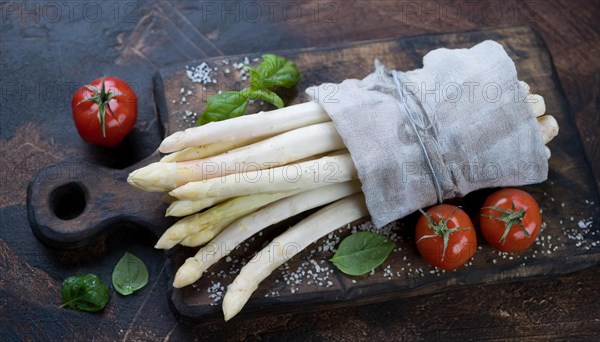 A bunch of asparagus next to ripe cherry tomatoes on a rustic background, bunch of white asparagus wrapped in a damp kitchen towel, KI generated, AI generated