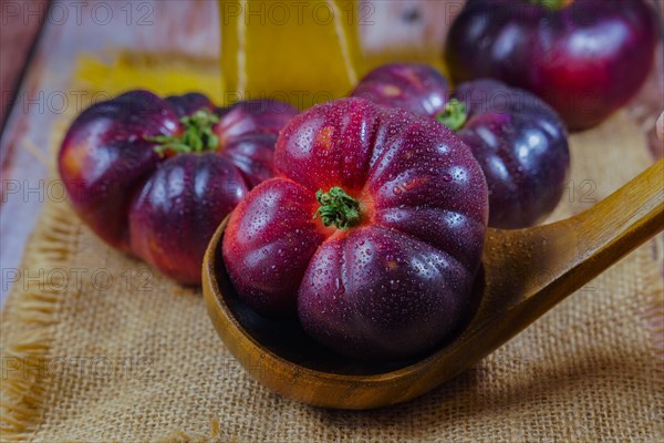 Close-up of an exquisite fresh blue variety tomato with raindrops on a wooden spoon