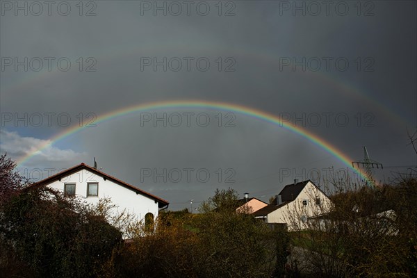 Rainbow over houses and electricity pylons against a blue sky