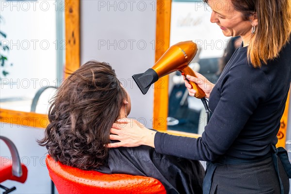 Rear view of a hairstylist drying the curly hair of a client in the salon