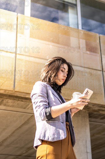 Young business woman walking down the street holding cell phone and glass of coffee, A Woman Walking Down The Street holding glass Coffee And Using Cell Phone