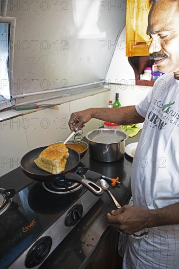 Indian man frying a dosa or pancake in a ship's galley, traditional Kerala dish, Kerala, India, Asia