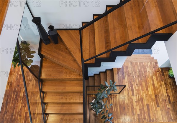 Top view of black powder coated steel L-shaped staircase with stained and varnished wooden steps and tempered glass handrail inside contemporary home with acacia wood flooring, Quebec, Canada, North America