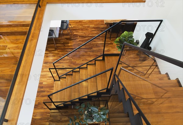 Top view of black powder coated steel L-shaped staircase with stained and varnished wooden steps and tempered glass handrail inside contemporary home with acacia wood flooring, Quebec, Canada, North America