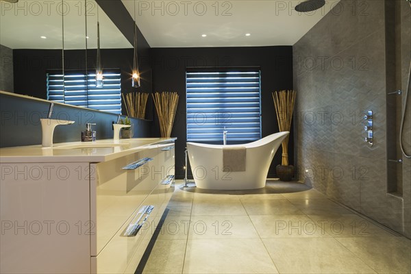 White high-gloss lacquered vanity with quartz countertop and his and her sunken sinks, freestanding high back soaking bathtub, Italian shower with rain head in en suite with grey nuanced ceramic tile floor inside contemporary home, Quebec, Canada, North America