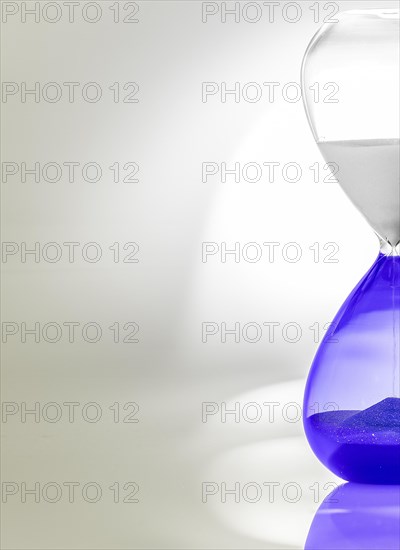 Hourglass with blue sand halfway through, minimalist design with shadows and reflections