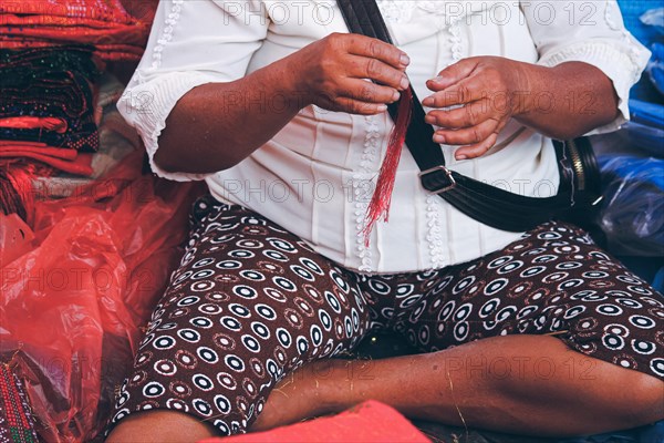 A tailor preparing red strands of threads by hand to make Ulos which is a traditional Tenun or weaving fabric of the Batak people of North Sumatra Indonesia