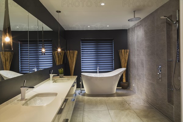 White high-gloss lacquered vanity with quartz countertop and his and her sunken sinks, freestanding high back soaking bathtub, Italian shower with rain head in en suite with grey nuanced ceramic tile floor inside contemporary home, Quebec, Canada, North America