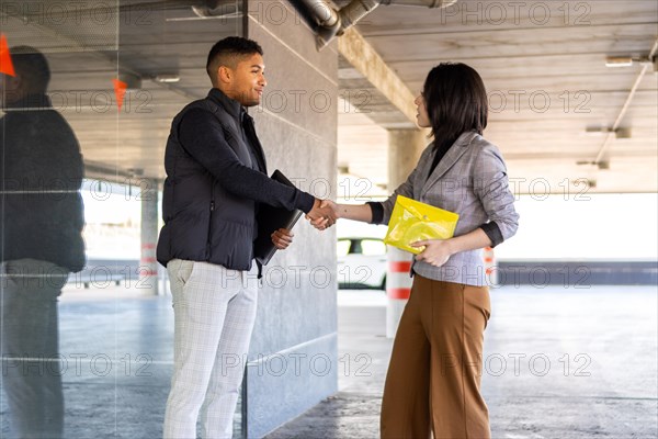 Woman in formal suit shaking hands with casual man outdoors. Business woman shaking hands with guy on the street