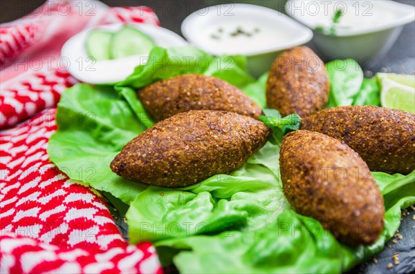 Delicious Lebanese (Arabic) food, kibbeh (kibe) with sauces and lemon on black slate stone and granite background with traditional keffyeh