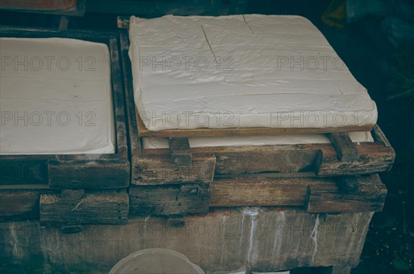 Overhead view of soy curd being pressed into wooden mold in a traditional Indonesian tahu or tofu factory that shows candid and authentic local product and livelihood