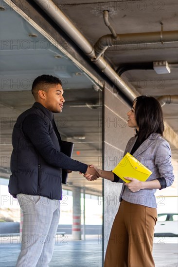 Woman in formal suit shaking hands with casual man outdoors. Business woman shaking hands with guy on the street