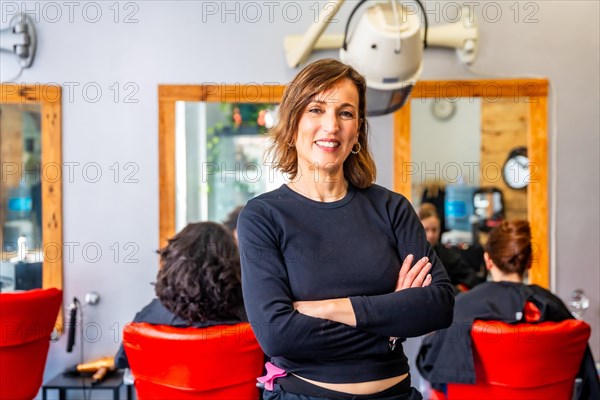 Portrait of a happy and proud hairdresser standing with arms crossed and smiling at camera in the salon