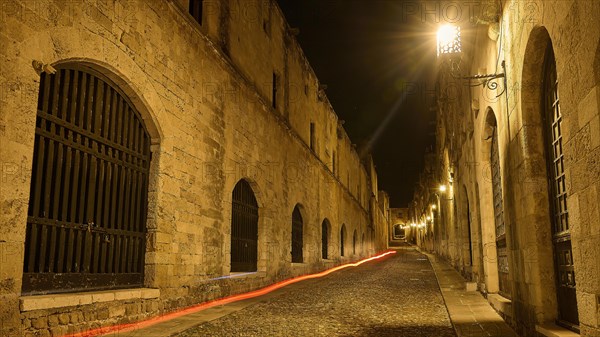 Quiet old stone street at night with warm lights leaving a harmonious impression, red light trail, knight street, night shot, old town of Rhodes, Rhodes town, Rhodes, Dodecanese, Greek Islands, Greece, Europe