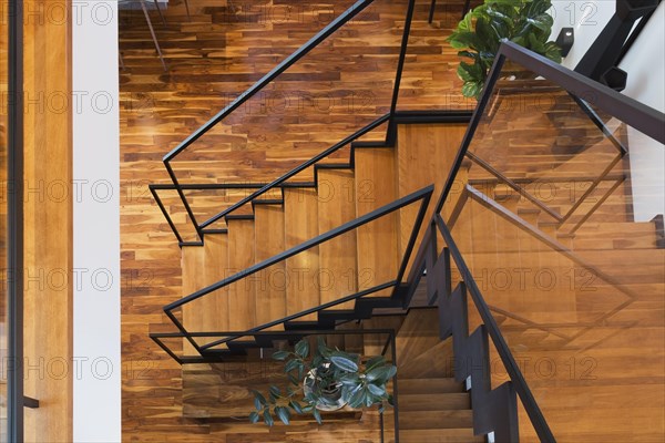 Top view of black powder coated steel L-shaped staircase with stained and varnished wooden steps and tempered glass handrail inside contemporary home with acacia wood flooring, Quebec, Canada, North America