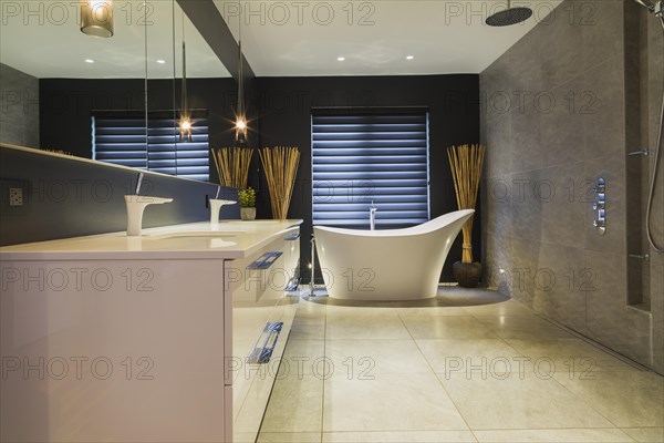 White high-gloss lacquered vanity with quartz countertop and his and her sunken sinks, freestanding high back soaking bathtub, Italian shower with rain head in en suite with grey nuanced ceramic tile floor inside contemporary home, Quebec, Canada, North America