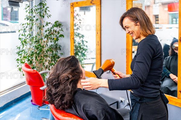 Hairstylist smiling while drying hair of a woman in the beauty salon