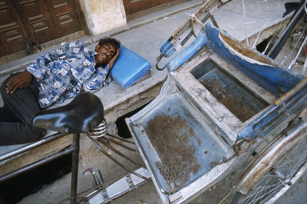 Man sleeping on the sidewalk. In the foreground, his rickshaw. Ajmer, Rajasthan, India, He is making a living from transporting people with his cycle rickshaw, Asia