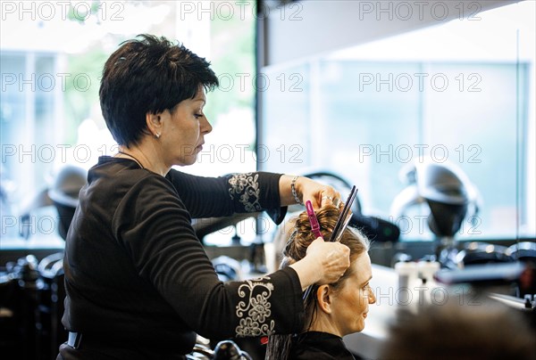 Valentyna Vysotska, hairdresser from Ukraine, puts up her customer's hair, photographed in the hairdressing salon Coiffeur Sivan in Berlin, 22/04/2024