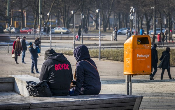 Young people sitting next to an orange-coloured waste bin of the Berlin city cleaning service, Germany, Europe