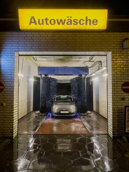 View of Fiat 500 in car wash at night with rotating brushes textile brushes for automatic machine car wash above illuminated sign with lettering car wash, Germany, Europe