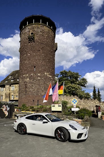 Porsche 911 GT3 stands in front of 13th century castle today Burghotel Trendelburg with castle tower, Trendelburg, Weserbergland, Hesse, Germany, Europe