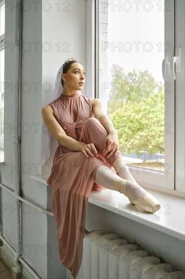 Ballerina sits thoughtfully on the windowsill and looks out the window during a break