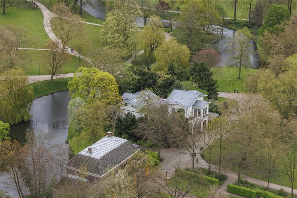 A dreamy picture of a park with buildings and a pond, surrounded by trees and paths, small park with green trees and paths between tall houses, Rotterdam, Netherlands