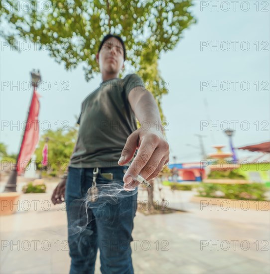 Portrait of guy smoking on the street. Close-up of a young man showing a lit cigarette on the street