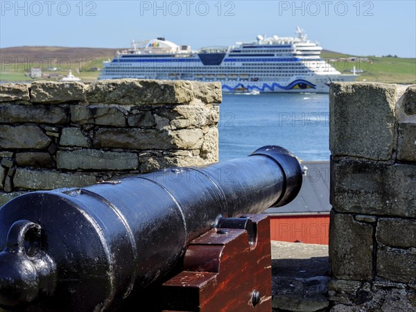 A cannon aims at a large cruise ship in the sea, old cannons on a stone wall by the sea against a blue sky, Lerwick, Scotland, United Kingdom, Europe