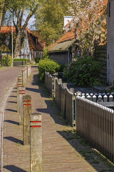 Quiet footpath along a wooden fence, lined with brick houses and trees in a village, historic houses and a church with small streets and lanterns, Nes, Ameland, Netherlands