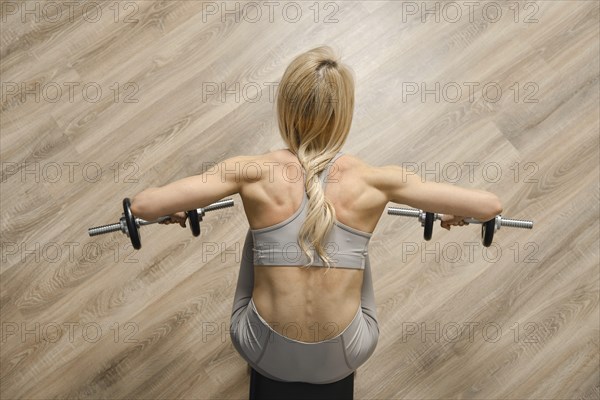 Top view of female bodybuilder pushing dumbbell to the sides while sitting on bench in gym