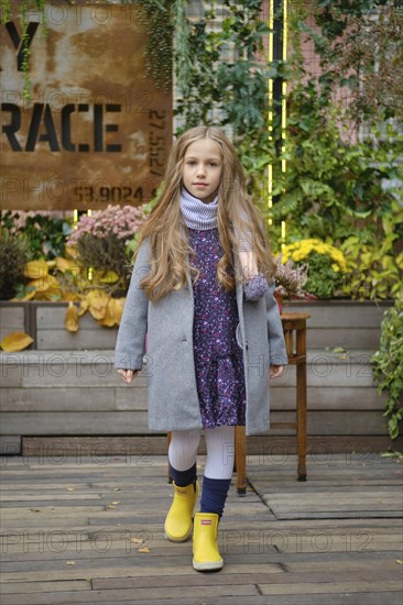 Little girl in coat, scarf and rubber boots walking on terrace