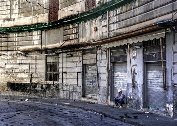 A man sits in front of a closed shop in the historic centre of Naples, 02/05/2024, Naples, Italy, Europe