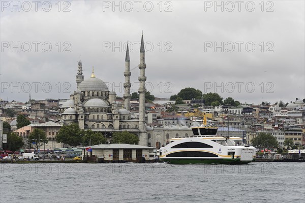 View of a mosque and a passing boat on the water in Istanbul on a cloudy day, Istanbul, Istanbul Province, Turkey, Asia