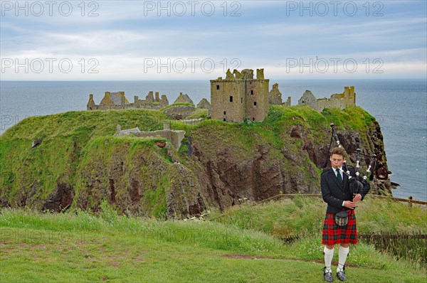 Bagpiper in front of the ruins of Dunnottar Castle, castle-like building on a cliff, Stonehaven, Scotland, Great Britain