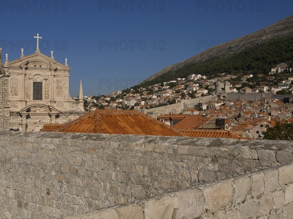 View over city walls and roofs to a church and surrounding mountains under a clear sky, the old town of Dubrovnik with historic houses, churches, red roofs and fortress walls, dubrovnik, coratia