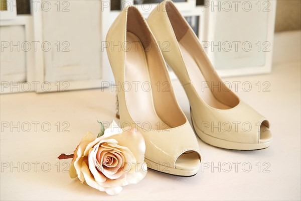 Beige high heels with peep-toe design next to a rose on a white background, B