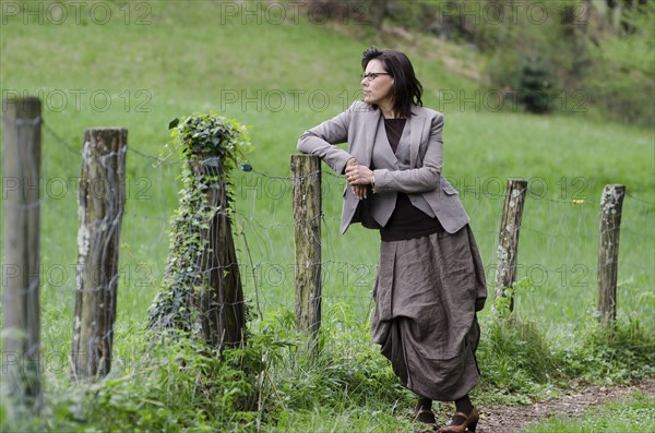 Elegant Business Woman Standing on a Forest Path and Leaning on a Fence in the Nature in Switzerland